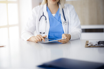 Unknown woman-doctor sitting in sunny clinic and using tablet pc, close-up. Data and best service in medicine