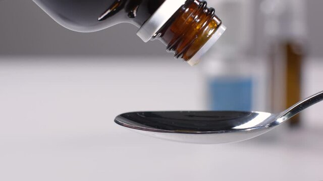 A small spoon is filled with cough drops from the medicine bottle.