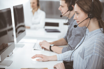 Call center. Group of casual dressed operators at work. Brunette business woman in headset at customer service office