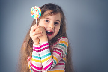 Little kid eating lollipop. Happy beautiful girl with candy isolated on blue background.