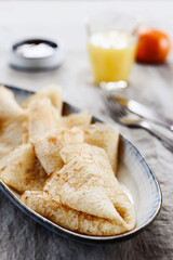 Breakfast with crepes or pancakes and jam, juice and tangerine on greige linen tablecloth. Pancake week or Shrovetide. Selective focus