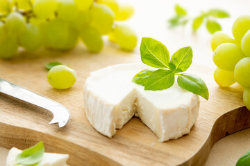 White wheel cheese with basil leaves. Goat cheese on wooden board with basil and grapes