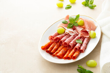 Meat assortment, salami slices in plate, with basil and grapes, copy space. Delicious snack for wine.
