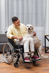 cheerful, disabled man hugging labrador while sitting in wheelchair