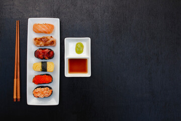 The sushi set is a famous Japanese dish, put on a ceramic plate, beautifully arranged on a black background.