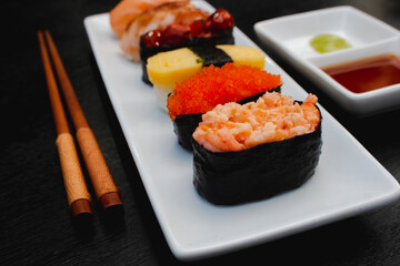 The sushi set is a famous Japanese dish, put on a ceramic plate, beautifully arranged on a black background.