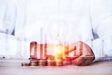 double exposure image concept, hand holding ligh blub coins idea business industrial technology future plant and enegry graphic design. Oil, gas and petrochemical refinery factory with background.