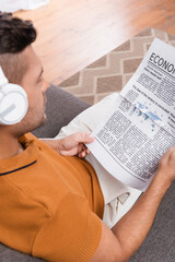 Naklejka premium overhead view of blurred man in headphones reading newspaper at home
