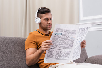 Naklejka premium young man reading newspaper while listening music in wireless headphones