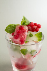 Close-up on ice with frozen berry and mint in the drinking glass on the gray background. Location vertical.