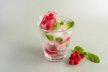 Ice with frozen berry and mint in the drinking glass on the gray background.  Copy space.