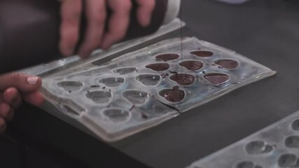 Close up shot of woman pouring fresh chocolate into heart molds.Cooking desserts from chocolate and cocoa