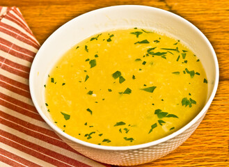 top view, close distance of asian egg drop soup with parsley in a round, white, bowl on a wooden serving board with a red and white stripped napkin