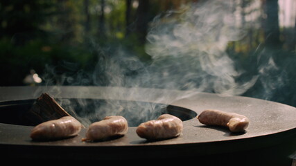 Unrecognized man putting sausages on bbq grill outdoors. Chef cooking sausages