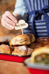 Sales Assistant In Bakery Putting Vegetarian Free Label Into Freshly Baked Baked Cinnamon Bun