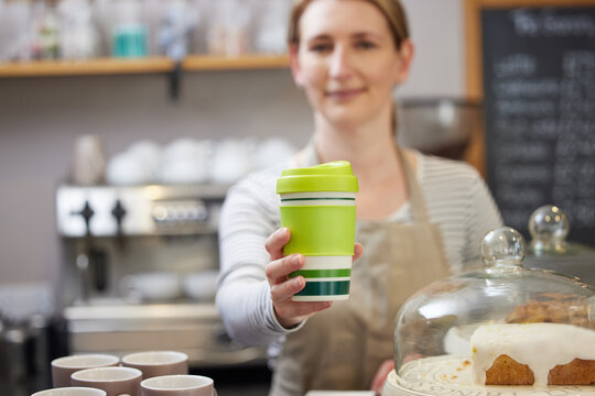Female Worker in Cafe Serving Coffee In Sustainable Reusable Cup