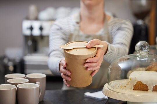 Close Up Of Female Worker in Cafe Serving Meal In Sustainable Recyclable Packaging With Wooden Spoon