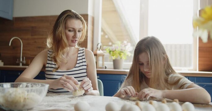 Mother and daughter spend time together baking in the kitchen at home. Young loving mom teach her daughter kneading dough. Cute kid learn to bake. Happy family have fun together at home.