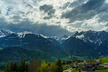 Bei Bartholomäberg auf der Alp, mit Blick auf den Rhätikon mit der Zimba und anderen verschneiten Bergen. Frühling mit blumenübersäten Wiesen und einer Sturmfront, die nach dem Föhn über das Tal kommt