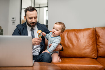 Young businessman dad working on a laptop at home while taking care of his newborn son. Multitasking and babysitter.