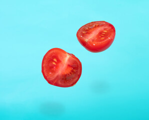 Minimal summer concept. Ripe red, halved cherry tomato tossed into the air. Levitation. bright blue background. - Powered by Adobe