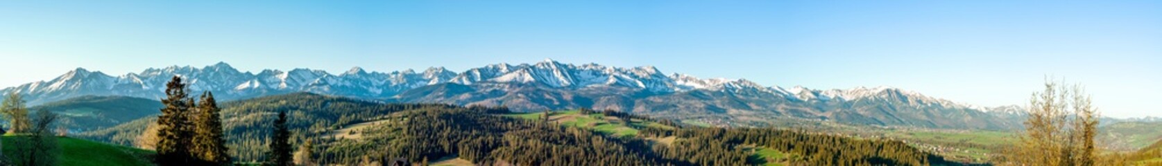 Extra wide panorama of the Tatra Mountains with trees, forests and meadows in Podhale region in Poland. Early morning in spring, sunrise light