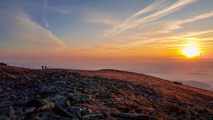 A panoramic view on sun rising above the horizon from the top of Babia Gora in Poland. Thick clouds below. The sky is pink and orange. A few small peaks popping out from the clouds. Freedom. Daybreak