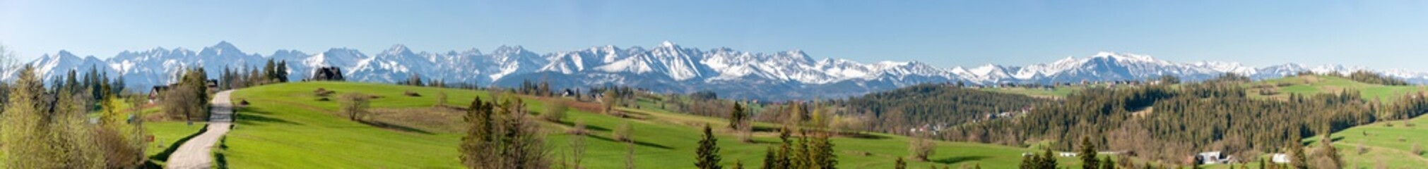 Wide panorama of  the Tatra Mountains in spring, with a village paved road, highlander houses, forests and green grass pasture