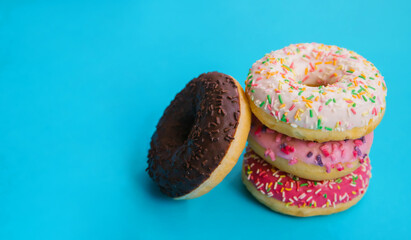 Sweet donuts of different colors lie on top of each other on a blue background.