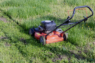 Obraz premium An old gasoline lawn mower mows the lawn. Side view.