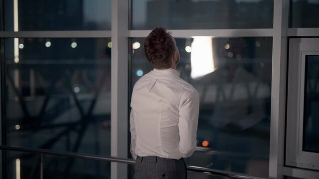 Rear view of adult business man standing by panoramic window on night city background