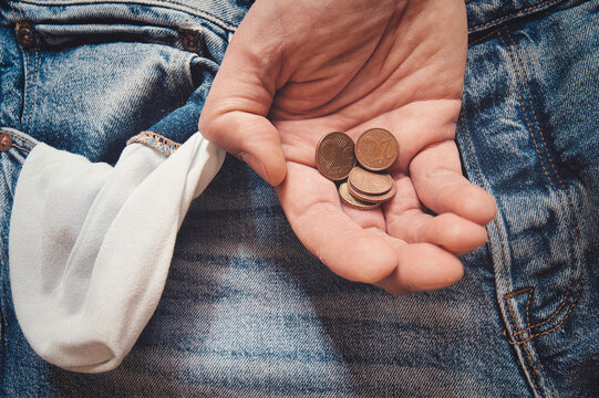 A Caucasian male holding a few coins over an empty pocket of his jeans- concept for saving