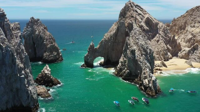 Aerial view of the Arch of Cabo San Lucas with some waves crashing in the rock, the drone slowly rotating.
