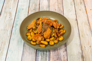 Green bowl with sautéed gnocchis in the Italian style with pieces of fried cheese and chopped chives