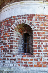 Arched window in the wall of the monastery. Old brickwork with remains of whitewash. Metal grill on the window.