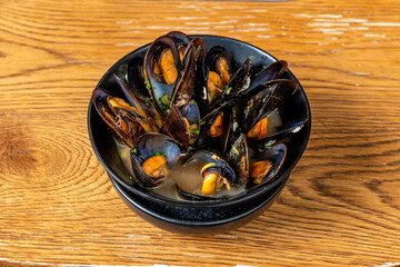 Black bowl with steamed mussels in their juice on wooden table