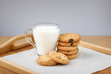 Cup of milk and cookies with raisins on a wooden tray