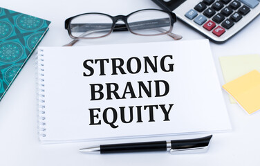 calculator, pen, glasses and notepad with text STRONG BRAND EQUITY in the white background