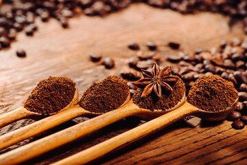 Wooden spoons filling of ground coffee on the old wooden table with coffee beans. Flower anise in one of the spoons.