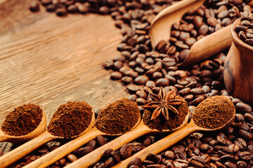 Wooden spoons filling of ground coffee on the old wooden table with coffee beans. Flower anise in one of the spoons.