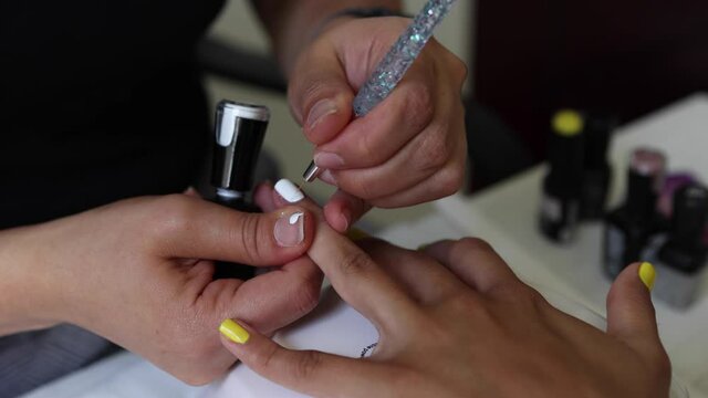Anonymous beautician applying lacquer on female client nails