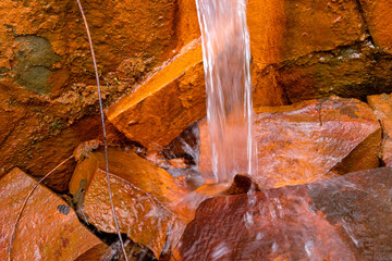 Water flow on red stones. The wild nature. Natural iron water in Ukraine. Long exposure. Wallpaper. Copy space. 