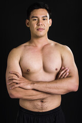 Fototapeta premium Asian strong healthy handsome muscular sportive man with shirtless, crossing arms, posing, looking at camera with confidence, standing on isolated black background.