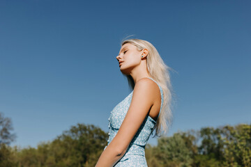 Fototapeta na wymiar Young woman with long blonde hair on blue sky background, outdoors.