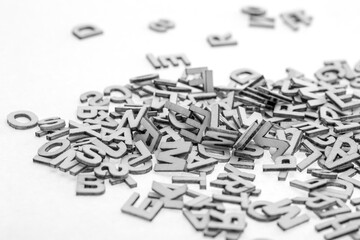 Small wooden letters cut from thin plywood with a laser cutter piled randomly in a pile on a white background. B&W photo.