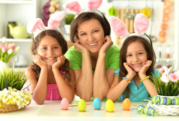  Mother with girls wearing rabbit ears decorating  Easter eggs