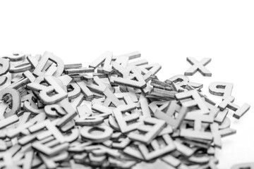 Small wooden letters cut from thin plywood with a laser cutter piled randomly in a pile on a white background. B&W photo.