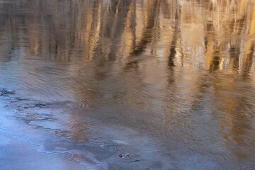 Winter landscape at sunrise of the Kalamazoo River with ice formation and reflections of trees in calm water, Michigan, USA