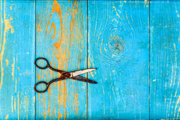 Rusty and ancient scissors disclosed on old wooden table covered with blue paint. View from above