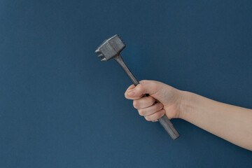 Female hand holds kitchen iron hammer for food preparation on dark green background, copy space. Creative food concept